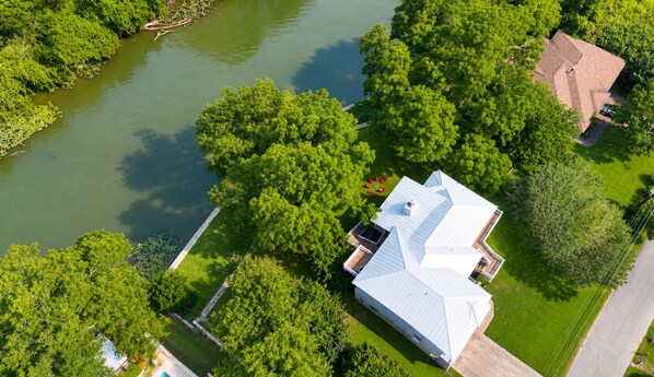 Luchtbeeld van een huis met een wit dak, omringd door weelderige begroeiing en een waterpartij.