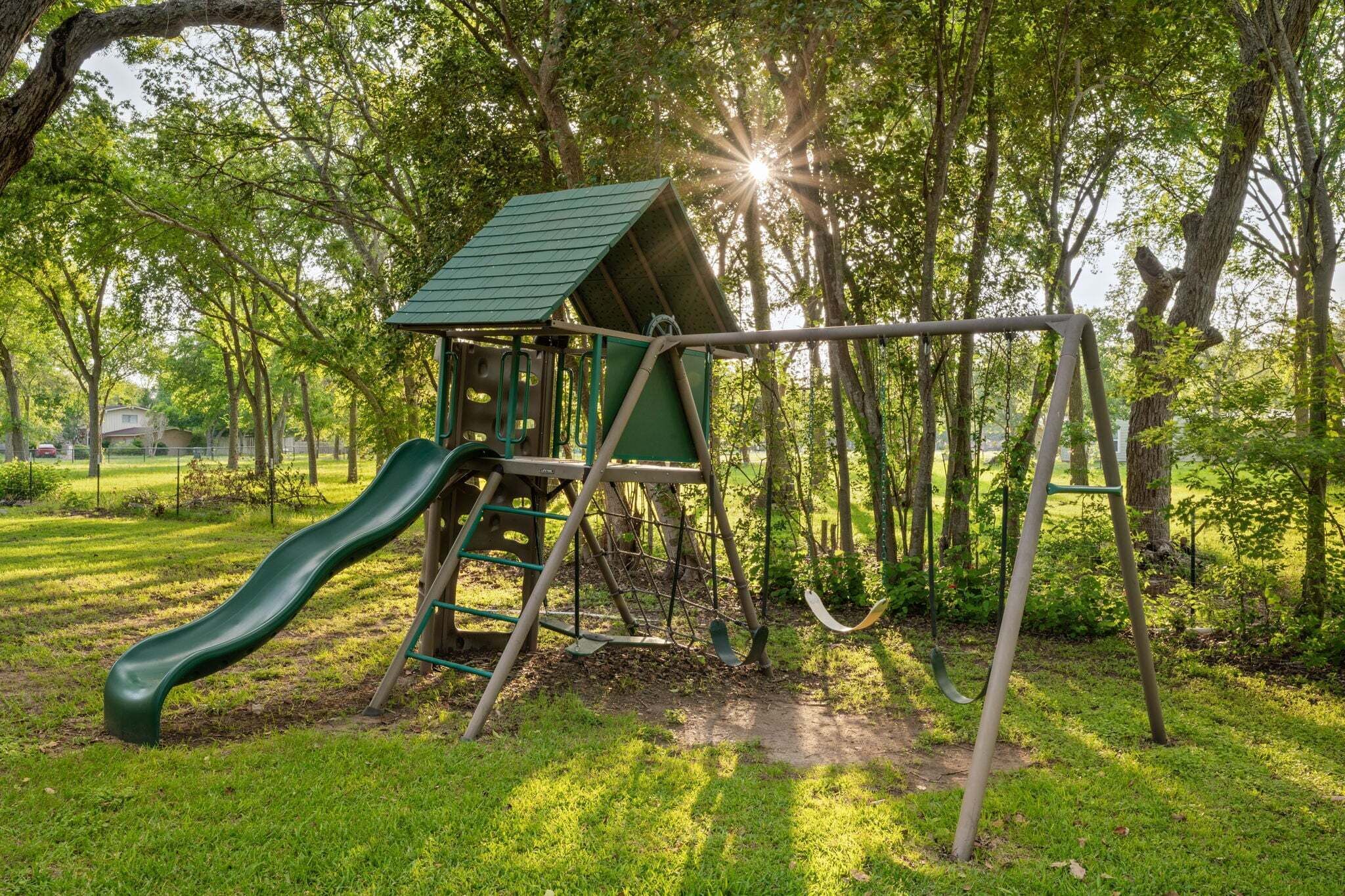 A playground with a slide and swings, surrounded by trees.