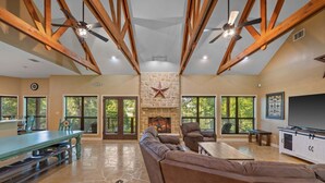 A spacious living room with a stone fireplace, leather sofas, a dining table, and large windows. - Winter Texan riverfront home on Lake Seguin with dock, kayaks, beautiful views & air hockey (Seguin)