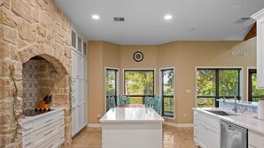 A kitchen with a stone arch, white cabinetry, a central island, and a view of the outdoors. - Winter Texan riverfront home on Lake Seguin with dock, kayaks, beautiful views & air hockey (Seguin)