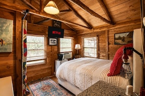 A cozy log cabin room with a bed, a lamp, a heater, and a sign indicating a Netflix service. - Modern Hill Country Multi-unit w/kitchen, WIFI, patio, private pool & hot tubs (Wimberley)