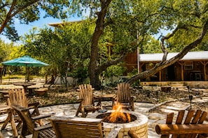 An outdoor seating area with wooden chairs and a fire pit. - Modern Hill Country Multi-unit w/kitchen, WIFI, patio, private pool & hot tubs (Wimberley)