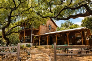 A rustic wooden building with a covered patio area, stone pathway, and outdoor seating. - Modern Hill Country house & rustic cabin with a private pool and hot tub (Wimberley)