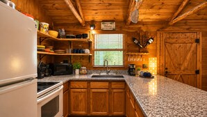 Una cucina in stile baita con pensili in legno, piani in granito, un frigorifero bianco, un fornello, un lavello e una finestra con persiane.