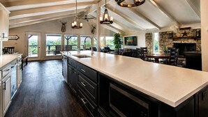A spacious kitchen with a large island, dark wood flooring, and a stone fireplace.