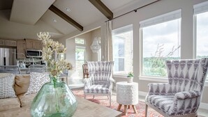 A spacious living room with a large window, patterned armchairs, a wooden coffee table, and a vase with flowers. - The All-Suite Century Oak House - Steps to Remi's Ridge & Hayes Hollow (Spring Branch)