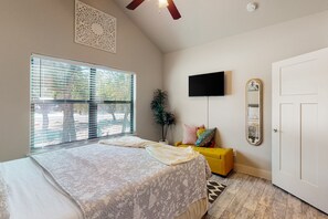 A bedroom with a bed, a TV mounted on the wall, a door, and a window with blinds. - Tanglewood Retreat | Updated house in Spring Branch with a large yard (Spring Branch)