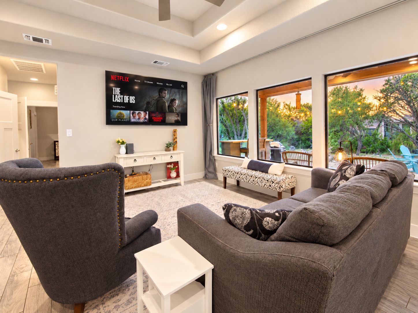 A modern living room with a sectional sofa, a white side table, and a flat-screen TV mounted on the wall displaying a movie.