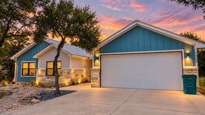 A two-story house with a garage, stone foundation, and a tree in the driveway. - Tanglewood Retreat | Updated house in Spring Branch with a large yard (Spring Branch)