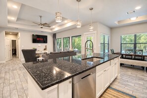 A modern kitchen with a large island, stainless steel appliances, pendant lighting, and a dining area with a view. - Tanglewood Retreat | Updated house in Spring Branch with a large yard (Spring Branch)