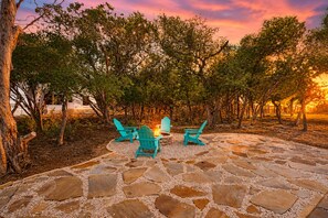 A patio with stone flooring and turquoise Adirondack chairs, surrounded by trees. - Tanglewood Retreat | Updated house in Spring Branch with a large yard (Spring Branch)