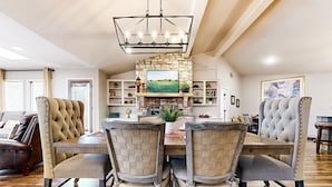 A dining area with a stone fireplace, wooden dining table, and tufted chairs. - Serene property with two living spaces and large outdoor space - dog-friendly (Wimberley)
