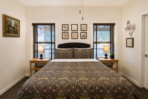 Un dormitorio con una cama grande, dos mesitas de noche con lámparas, un cabecero y varias fotografías enmarcadas en las paredes.