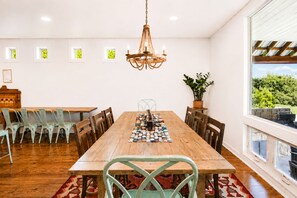 Un comedor con una mesa de madera, sillas, una araña y vistas a la vegetación exterior.