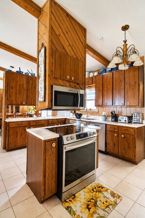 A kitchen with wooden cabinets, a microwave, a stove, and a chandelier. - Cozy 3BR in Canyon Lake | Grill | Private Backyard and Winter Texan Friendly (Canyon Lake)