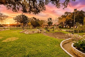 A landscaped garden with a fence, a bird feeder, and a building in the background. - Sunny home with covered patio, grill, beautiful views, lawn, streaming, W/D, AC (Canyon Lake)