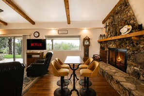 A living room with a stone fireplace, a television displaying 'NETFLIX,' a dining table, and two leather chairs. - Cozy 3BR in Canyon Lake | Grill | Private Backyard and Winter Texan Friendly (Canyon Lake)