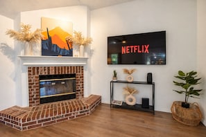 Un soggiorno con camino in mattoni, televisione a parete e oggetti decorativi.