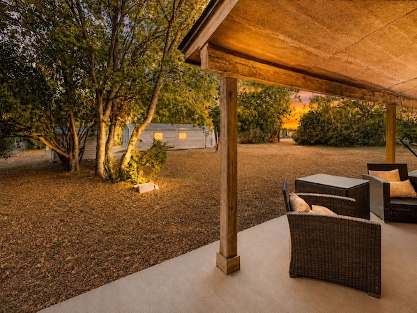 Un patio coperto con mobili in vimini, pavimento in cemento e alberi sullo sfondo.