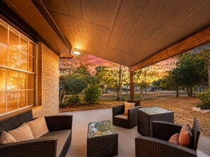 An outdoor patio with wicker furniture, a brick wall, and a view of trees and a sunset.