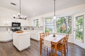 Une cuisine moderne avec des meubles blancs, un îlot central et un coin repas comprenant des chaises et une table en bois.