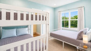 Une chambre avec des lits superposés, une fenêtre avec des rideaux et une table de chevet avec une lampe.