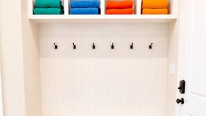 Une pièce avec un banc blanc, une étagère fixée au mur où sont pliées des serviettes, et une porte avec une poignée noire.