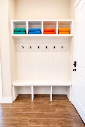 Une pièce avec un banc blanc, une étagère fixée au mur où sont pliées des serviettes, et une porte avec une poignée noire.