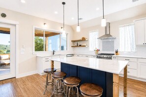 Une cuisine moderne dotée d’un grand îlot central, de tabourets de bar, de luminaires suspendus et offrant une vue sur l’extérieur.