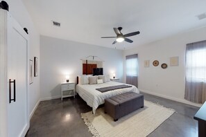 A bedroom with a bed, bedside tables, a bench, a ceiling fan, and a large window with curtains. - Secluded home with firepit, gas grill, central AC, game room, W/D (Fischer)