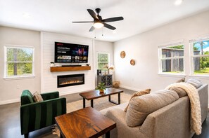 Ein Wohnzimmer mit Kamin, einem an der Wand montierten Fernseher, einem Deckenventilator und einem Sofa.