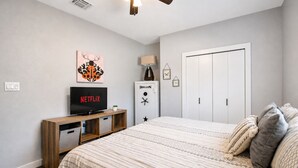 Une chambre à coucher avec un lit, un téléviseur posé sur un meuble en bois, une armoire et une porte.