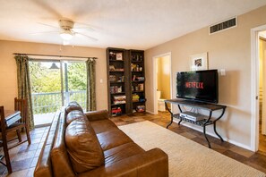 Un soggiorno con un divano in pelle, una libreria, un televisore che mostra 'NETFLIX' e un balcone con tende.