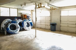 Un garage con pavimento in cemento, una porta bianca e una mensola in legno con diversi oggetti.