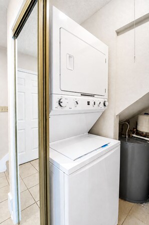 A compact laundry room with a front-loading washer and dryer, a white door, and a grey trash can. - Two-Story Golf Course Front Condo w/Balconies, Free WiFi, Gas Grill, Central A/C (Canyon Lake)