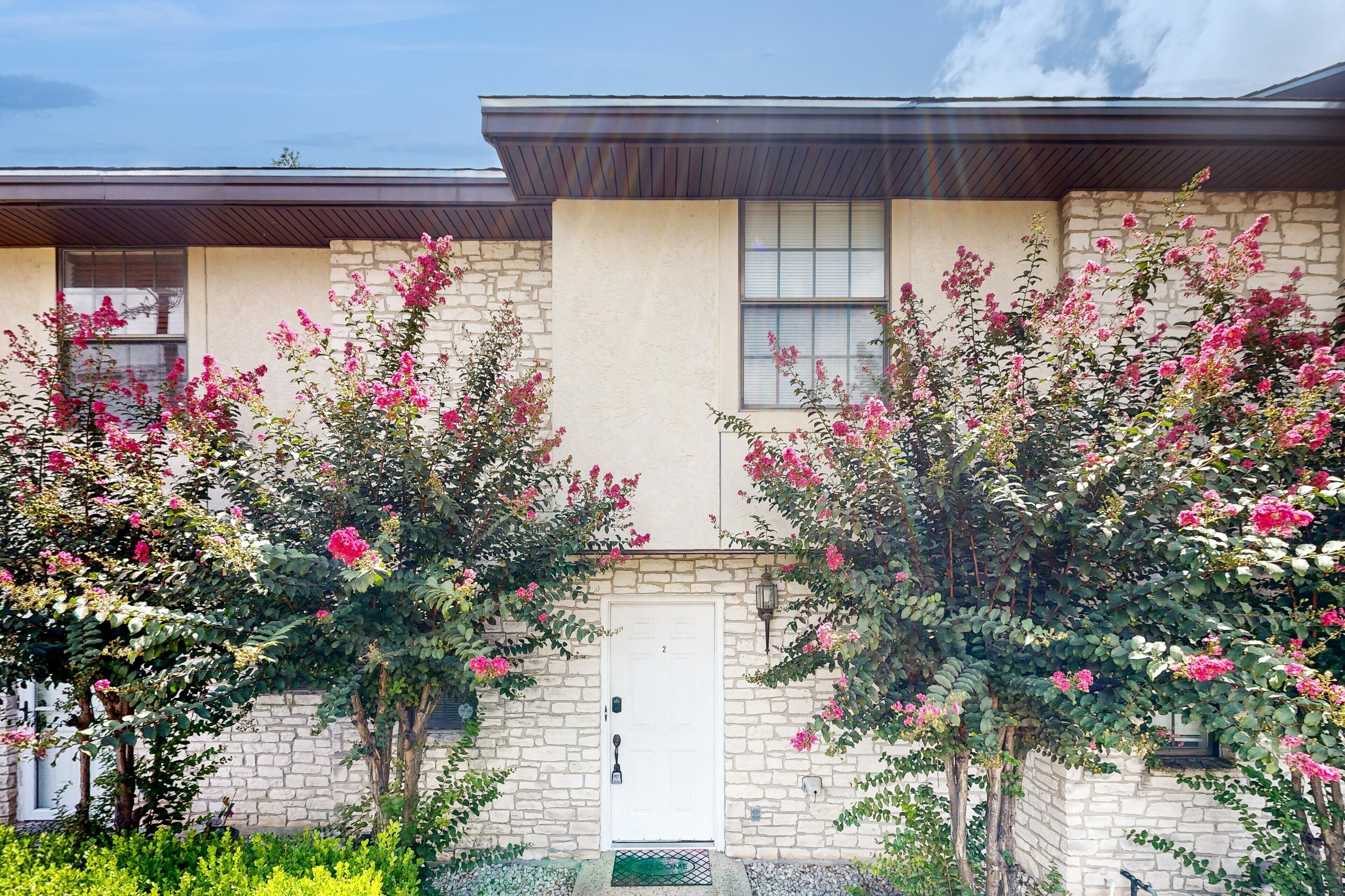 A two-story building with a stone facade, a white door, and pink flowering trees in front.