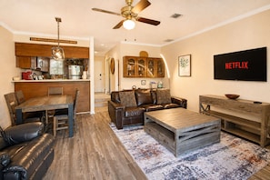 A living room with a brown leather sofa, a wooden coffee table, and a TV mounted on the wall. - Two-Story Golf Course Front Condo w/Balconies, Free WiFi, Gas Grill, Central A/C (Canyon Lake)