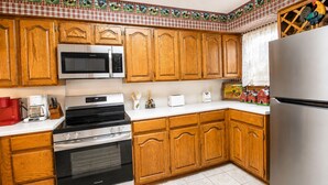 Una cocina con gabinetes de madera, un refrigerador de acero inoxidable, un microondas, un horno y una cafetera.