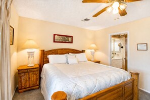 A bedroom with a wooden bed, two bedside tables with lamps, a ceiling fan, and a door leading to a bathroom. - Two-Story Golf Course Front Condo w/Balconies, Free WiFi, Gas Grill, Central A/C (Canyon Lake)