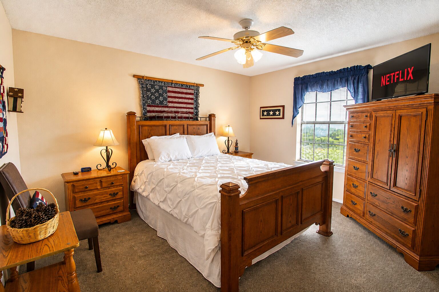 A bedroom with a wooden bed, a ceiling fan, a TV, a wardrobe, and a window with curtains.