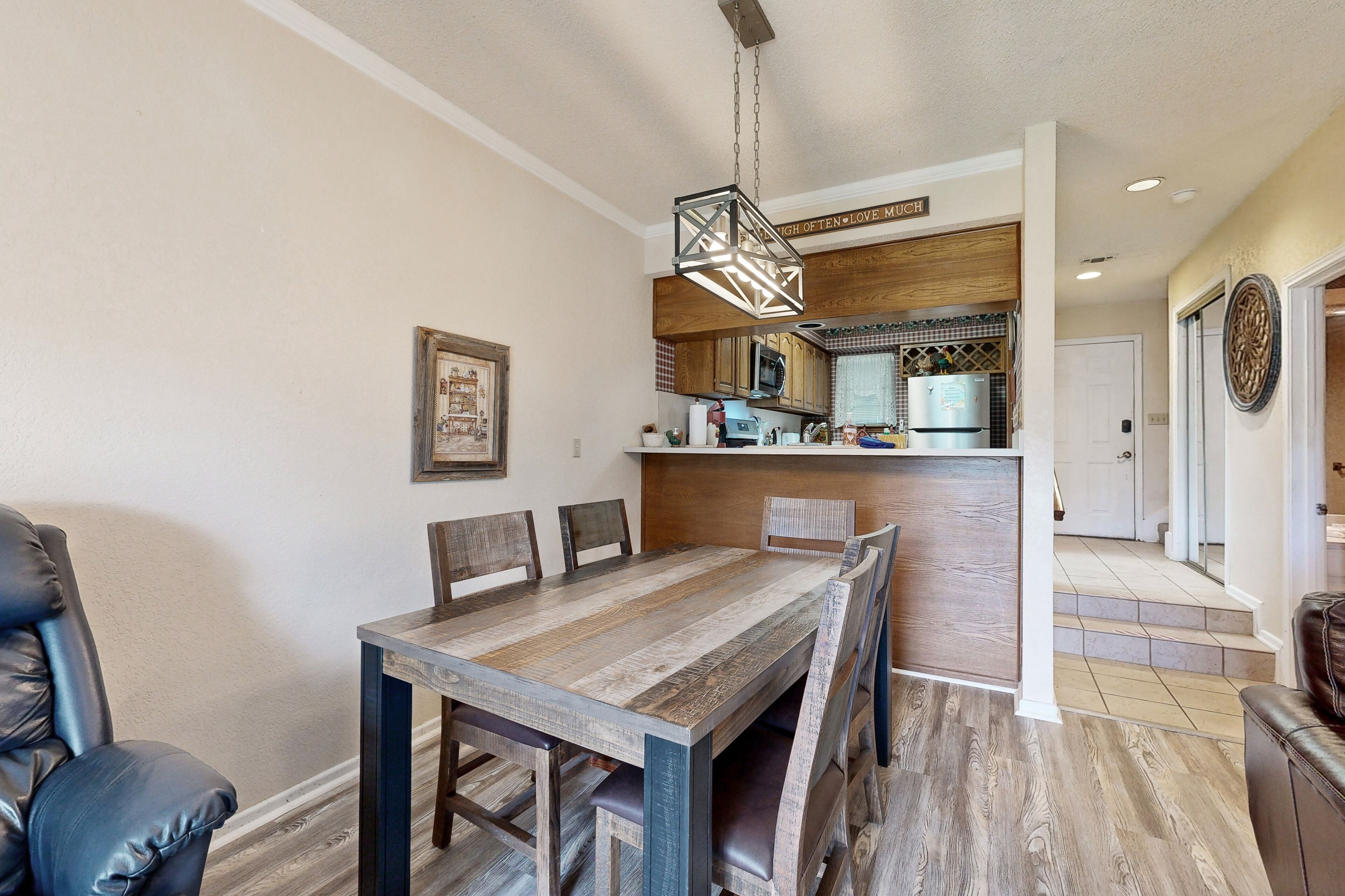 Un coin repas avec une table et des chaises en bois, un luminaire suspendu et une cuisine en arrière-plan.