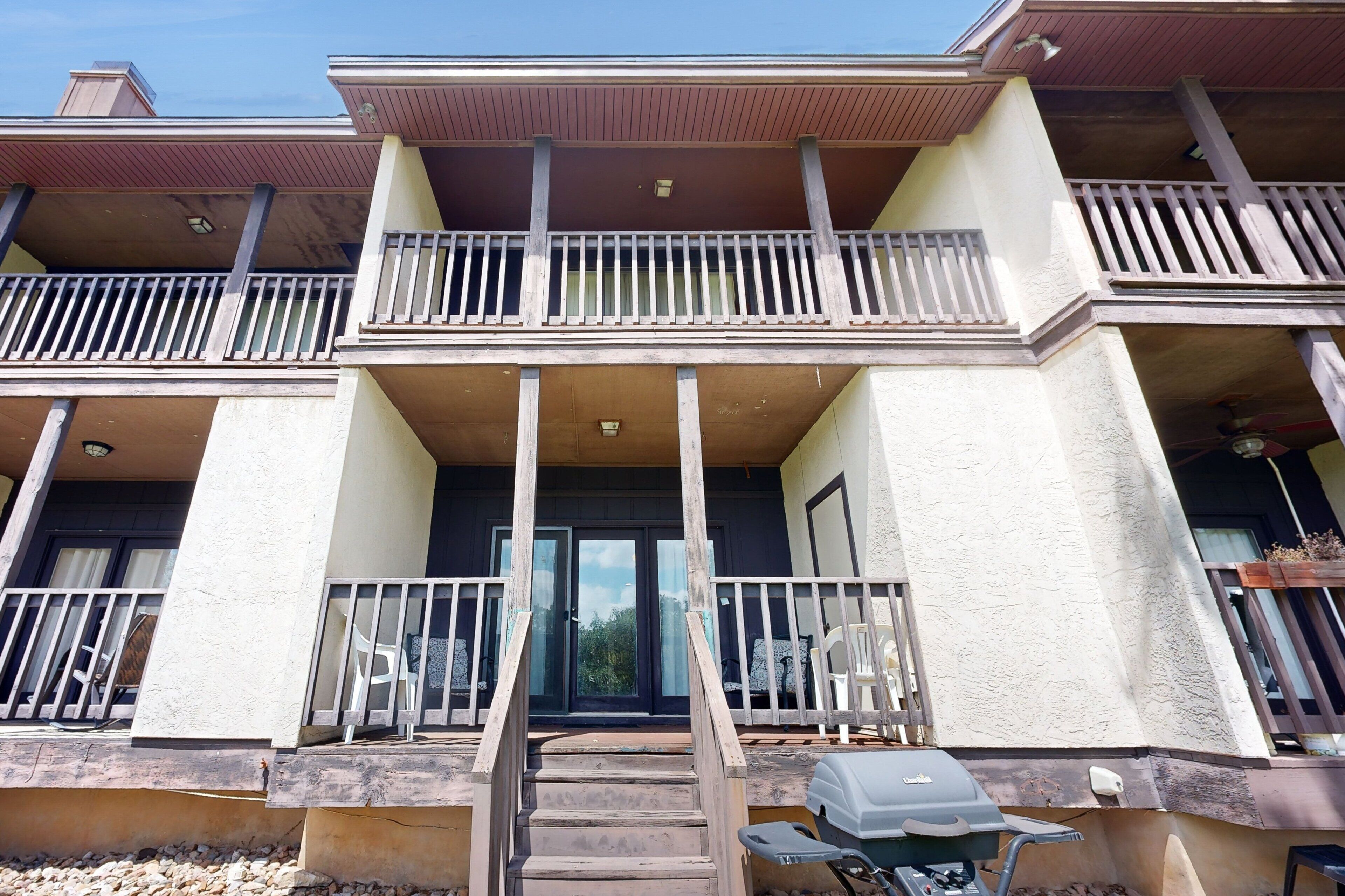 Un bâtiment à deux étages doté d’un balcon à l’étage supérieur, d’un escalier menant à l’entrée et d’un barbecue à l’extérieur.