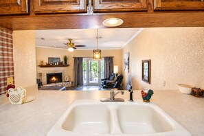 A kitchen with a double sink, a ceiling fan, and a fireplace in the background.