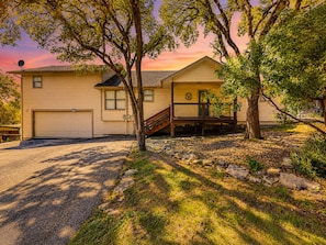 A two-story house with a garage, a covered porch, and a staircase leading to the second floor. - Quiet, private retreat with lake views, huge covered deck, W/D, & fenced yard (Canyon Lake)