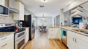 Une cuisine moderne équipée d’appareils électroménagers en acier inoxydable, un coin repas avec une table et des chaises, et une vue sur le salon.