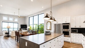 A modern kitchen with a large island, white cabinetry, stainless steel appliances, and a dining area with a view. - Modern lakefront home with multi levels and gorgeous views and Winter Texan Friendly (Canyon Lake)