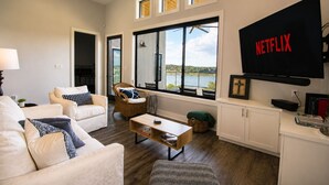 A living room with a sofa, armchair, coffee table, and a TV mounted on the wall. - Modern lakefront home with multi levels and gorgeous views and Winter Texan Friendly (Canyon Lake)