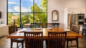 A dining area with a large window, wooden table, chairs, and kitchen appliances. - Modern lakefront home with multi levels and gorgeous views and Winter Texan Friendly (Canyon Lake)