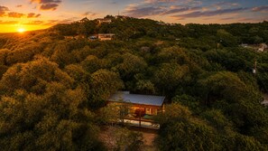 Ein eingeschossiges Haus, umgeben von dichtem Wald, mit freiem Blick auf den Sonnenuntergang im Hintergrund.