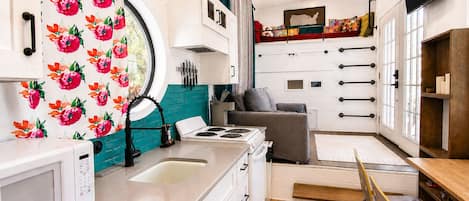 A compact kitchen with a microwave, sink, stove, and a dining area with a bench and chairs.